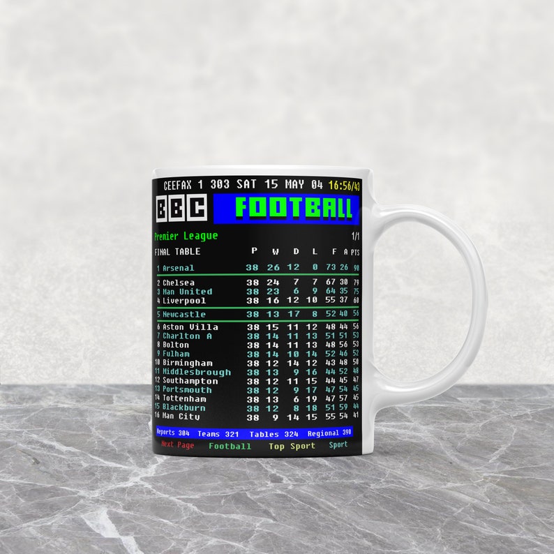 K&ouml;nnte beinhalten: Wei&szlig;e Keramik-Tasse mit einem Retro-BBC-Fu&szlig;ball-Grafik, die eine Abschlusstabelle der Premier League zeigt. Die Tasse zeigt die Team-Wertungen, einschlie&szlig;lich Arsenal, Chelsea und Manchester United, mit Datum und Uhrzeit.