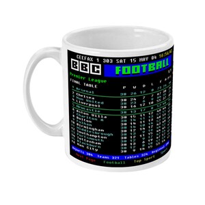 K&ouml;nnte beinhalten: Wei&szlig;er Keramikbecher mit einer Premier League-Abschlusstabelle von BBC Football. Der Becher zeigt die Team-Wertungen, einschlie&szlig;lich Arsenal, Chelsea und Manchester United, in einem Retro-Pixel-Stil. Der Becher hat einen wei&szlig;en Griff.