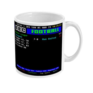 Op de afbeelding: Witte keramische mok met een zwarte afbeelding met het woord "FOOTBALL" in blauw, een score van 7-0 tussen Liverpool en Man United en het BBC-logo. De mok toont ook wedstrijddetails.