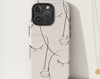 May include: A beige phone case featuring a black line art design of abstract faces. The case is next to a gold necklace with a small circular pendant and a spiral-bound notebook.