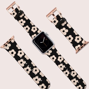 Op de afbeelding: Een zwart leren horlogebandje met een wit bloemenpatroon en ros&eacute;gouden hardware. Het bandje wordt in drie verschillende posities getoond, waaronder op een zilveren horlogewijzerplaat.