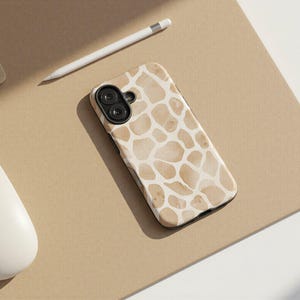 May include: A smartphone case with a giraffe print design in shades of beige and white. The case is lying on a tan surface next to a white mouse, a white pencil, and a keyboard.