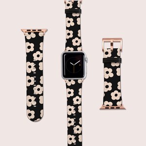 Op de afbeelding: Een zwart-witte Apple Watch band met een bloemenpatroon, een ros&eacute;gouden wijzerplaat en een zilveren Apple Watch.