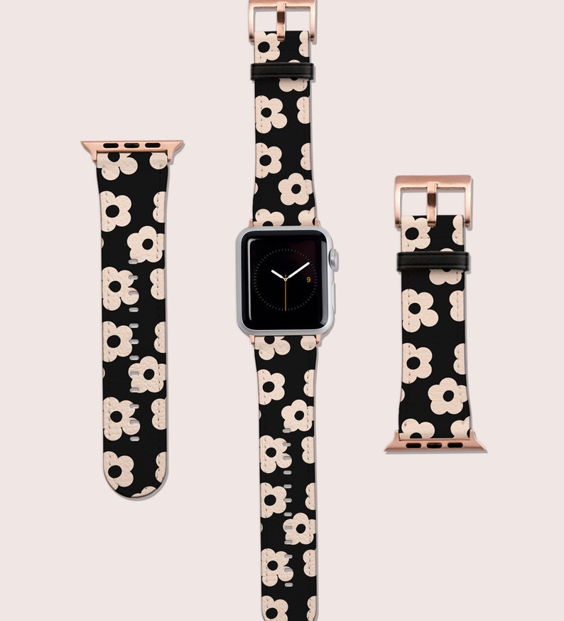 Op de afbeelding: Een zwart-witte Apple Watch band met een bloemenpatroon, een ros&eacute;gouden wijzerplaat en een zilveren Apple Watch.
