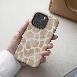 May include: A smartphone case with a giraffe print design. The case features a pattern of irregular brown shapes on a white background. The phone case has a black border and a camera module with three lenses.