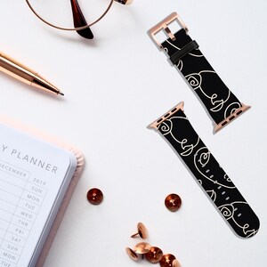 May include: Two black and white Apple Watch bands with rose gold hardware. The bands feature a repeating pattern of abstract faces.
