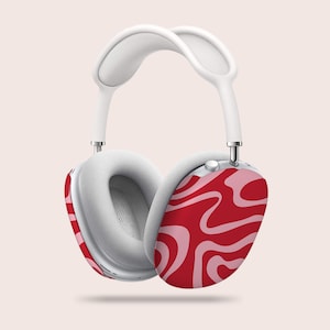 Puede incluir: Auriculares blancos sobre la oreja con un patr&oacute;n de remolino rojo y rosa en los auriculares. La diadema y las almohadillas son blancas. Los auriculares est&aacute;n suspendidos sobre un fondo rosa claro.