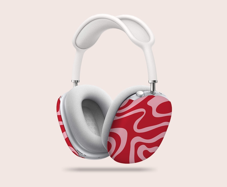 Puede incluir: Auriculares blancos sobre la oreja con un patr&oacute;n de remolino rojo y rosa en los auriculares. La diadema y las almohadillas son blancas. Los auriculares est&aacute;n suspendidos sobre un fondo rosa claro.