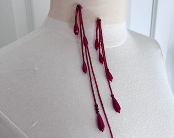 May include: A pair of long, dangling earrings with multiple strands of burgundy beads and teardrop-shaped accents.