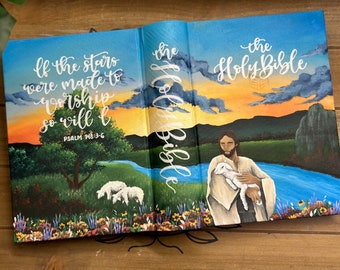 May include: A painted wooden Bible with a sunset scene on the cover. The text "If the stars were made to worship so will I" is written on the front cover with the scripture reference "Psalm 148:3-6". The back cover features a painting of Jesus holding a lamb with the text "the Holy Bible" written in cursive.