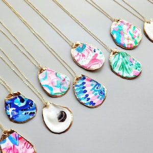 May include: A collection of gold chain necklaces with oyster shell pendants. The shells are painted with various floral patterns in shades of pink, blue, and green.