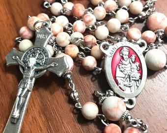 May include: A white and red marbled stone rosary with a silver chain and a silver crucifix with a depiction of Jesus Christ. The rosary also features a silver medal with a depiction of Saint Anthony of Padua.