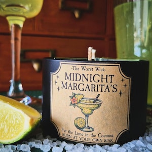 May include: A black candle in a cylindrical container with a tan label featuring the text The Worst Wick MIDNIGHT MARGARITA'S Put the Lime in the Coconut BURN AT YOUR OWN RISK and an illustration of a margarita glass with a lime wedge.