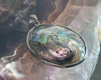 May include: A silver pendant featuring a round iridescent abalone shell with a textured surface. The shell has shades of green, blue, purple, and brown.