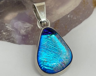 May include: A teardrop-shaped pendant with a blue and purple dichroic glass inlay set in a silver frame.