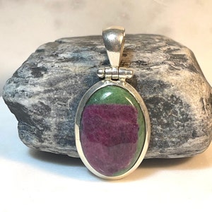May include: A silver pendant with a green and pink oval gemstone. The pendant is set in a silver bezel and has a bail for attaching a chain.