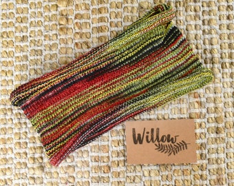 May include: A multi-colored striped knitted headband in shades of red, green, black, and white. The headband is on a woven straw background with a brown tag that says "Willow" with a stylized fern leaf.