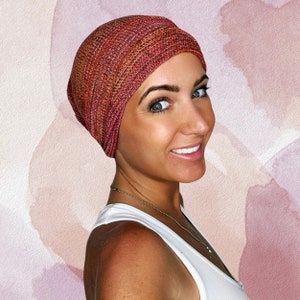 May include: A woman wearing a red and orange knit beanie hat. The hat is made of a soft, stretchy fabric and has a slouchy fit.