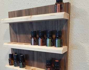 May include: A wooden shelf with multiple tiers for storing essential oil bottles. The shelf is made of light and dark wood and has a rounded edge. The bottles are all labeled with the word "OTERRA" and have different colored labels.