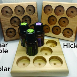 May include: Three wooden trays with nine round indentations each, designed to hold essential oil bottles. The trays are made of sugar maple, hickory, and poplar wood. The trays are displayed on a white surface with three essential oil bottles in the center.