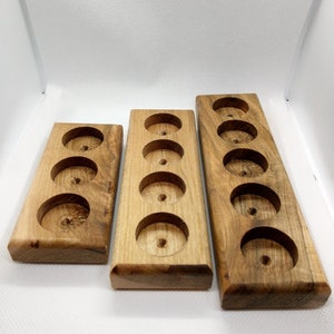 May include: Three wooden trays with circular cutouts. The trays are made of light brown wood with a natural finish. The trays are different sizes, with the largest tray having six cutouts, the middle tray having five cutouts, and the smallest tray having four cutouts.