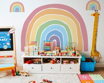 Puede incluir: Un adhesivo de pared de arcoíris colorido con un estante de madera para juguetes debajo. El estante está lleno de juguetes de madera coloridos, incluyendo bloques, ábaco y una jirafa para medir la altura.