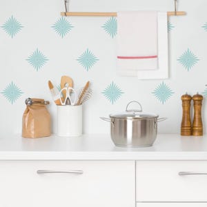 May include: A white kitchen with a stainless steel pot, a white ceramic utensil holder with wooden kitchen utensils, and two wooden salt and pepper shakers. The wall is decorated with light blue starburst decals.