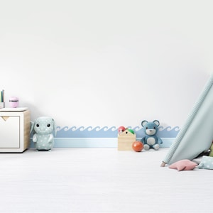 May include: A white wall with a blue wave border, a light blue teepee tent, a blue teddy bear, a light blue bunny, a wooden box with red and green balls, and a red ball on the floor.