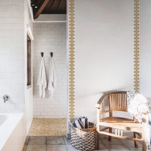May include: A white tiled bathroom with a wooden bench and a wicker basket. The walls have a decorative gold geometric pattern.