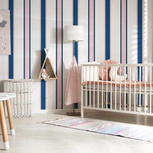 May include: A nursery with a white crib, a striped wall with blue and pink vertical lines, and a white wicker basket. A wooden teepee-shaped shelf holds a doll. A floor lamp with a white shade and a pink blanket are also visible.