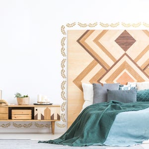 May include: A bedroom with a wooden headboard featuring a geometric pattern. The headboard is decorated with a gold leaf garland border. The bed is made with a teal green blanket and a light blue duvet.
