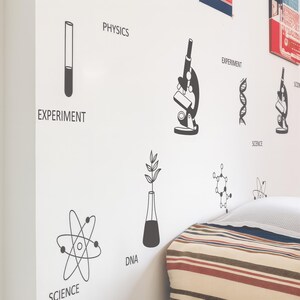 May include: A white wall decorated with black science-themed decals. The decals include a microscope, DNA strands, an atom model, and text labels such as "Physics," "Experiment," "Science," and "DNA." A striped pillow is visible in the bottom right corner.