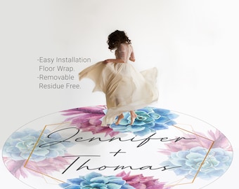 May include: A round, white floor wrap with a watercolor design of blue and pink succulents. The text "Jennifer + Thomas" is written in black script on the floor wrap.