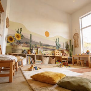 K&ouml;nnte beinhalten: Ein Kinderspielzimmer mit einer Wandtapete im W&uuml;sten-Design mit Kakteen und Sonne, einem niedrigen Holzregal voller B&uuml;cher und Spielzeug, einem hellen Teppich, zwei Bodenkissen in Senfgelb und Olivgr&uuml;n sowie einem kleinen Holztisch.