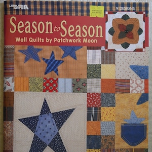 May include: A book titled "Season to Season" featuring patchwork quilt designs. The cover features a quilt with a large blue star in the center and a smaller blue star in the upper left corner. The book is by Patchwork Moon.