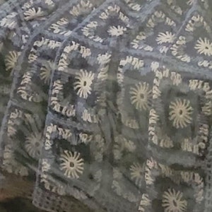 May include: A close-up of a crocheted blanket with a blue and white pattern. The blanket is made of a soft, textured yarn and features a repeating design of flowers.