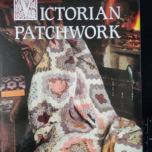 May include: A book titled "Victorian Patchwork" by Freda Parker, featuring a colorful patchwork quilt draped over a wooden chair in front of a fireplace.