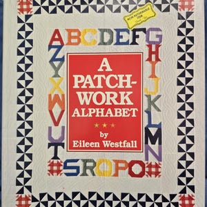May include: A book cover with a red background and white text that reads "A Patch-Work Alphabet" by Eileen Westfall. The cover is decorated with a patchwork alphabet border in various colors.