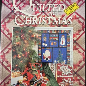May include: Book cover for "Quilted for Christmas" book II. The cover features a red and white patchwork design with a Christmas tree and a quilt with a snowman, Santa Claus, and other Christmas motifs.