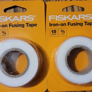 May include: Two rolls of white Fiskars Iron-on Fusing Tape, each measuring 15 yards by 3/4 inch, packaged on orange cards.