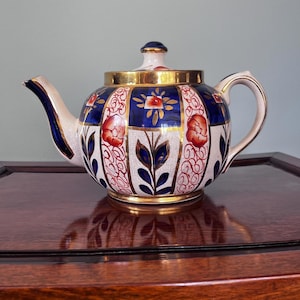 May include: A trio of cream-glazed ceramic mugs with a speckled finish. Each mug is adorned with a hand-painted design: a blue and green leaf, a yellow flower, and a red berry. The mugs have a simple, rounded form.