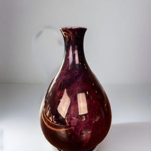 May include: A dark purple and gold ceramic vase with a round body and a narrow neck. The vase has a marbled effect with swirls of gold and purple.