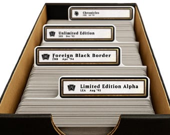 May include: A black storage box filled with stacks of trading cards separated by white dividers. The dividers feature labels for Limited Edition Alpha, Foreign Black Border, Unlimited Edition, and Chronicles, each with specific set codes and dates.