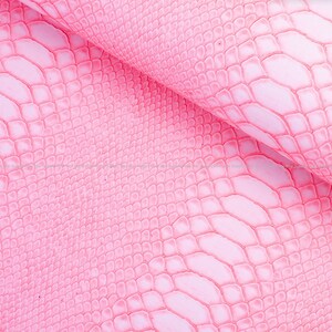 May include: Close-up of pink faux leather with a reptile scale pattern. The material is folded, revealing the texture and colour variations. The surface has a glossy finish, and the scales are raised, creating a three-dimensional effect. Ideal for crafting.