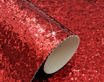 Op de afbeelding: Een rol rode glitterstof. De stof is bedekt met kleine, sprankelende rode pailletten, die het licht vangen en een glinsterend effect creëren. De onderkant van de stof is lichtbeige.