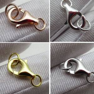 May include: Four metal lobster claw clasps in rose gold, silver, gold, and gunmetal. Each clasp has a spring-loaded mechanism and a small connecting ring. The clasps are shown against a light gray fabric background.