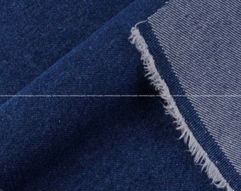 May include: Close-up of a folded piece of dark blue denim fabric. The fabric has a textured surface and a frayed edge, revealing the lighter-colored interior. The denim is a classic material for clothing and accessories.
