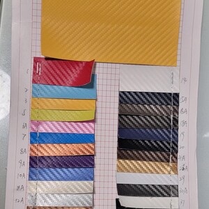 Peut inclure: Échantillons texturés en fibre de carbone de différentes couleurs, dont jaune, rouge, bleu, vert, rose, orange, violet et argent. Les échantillons sont disposés sur un fond de papier quadrillé, mettant en valeur le tissage du matériau.