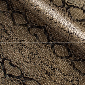 Op de afbeelding: Close-up van een textiel met een slangenleerpatroon. Het materiaal is een mix van goud- en bruintinten, met donkerbruine en zwarte accenten die het schubeffect creëren. De stof is gevouwen en toont zijn textuur.