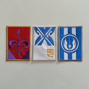 May include: Three embroidered patches with different designs. The first patch is red with a purple symbol, the second is white with a blue symbol and the third is blue with a white symbol.